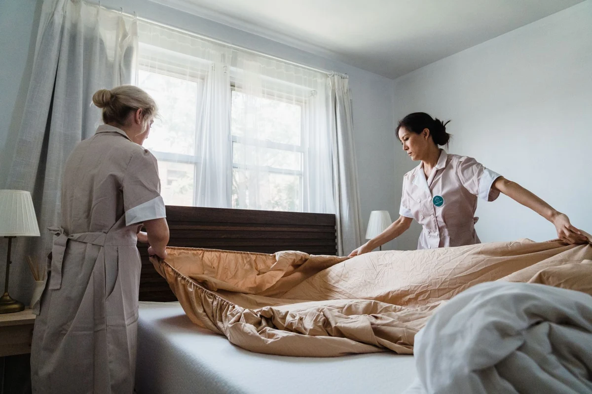 Two people fitting fresh sheets over a bed