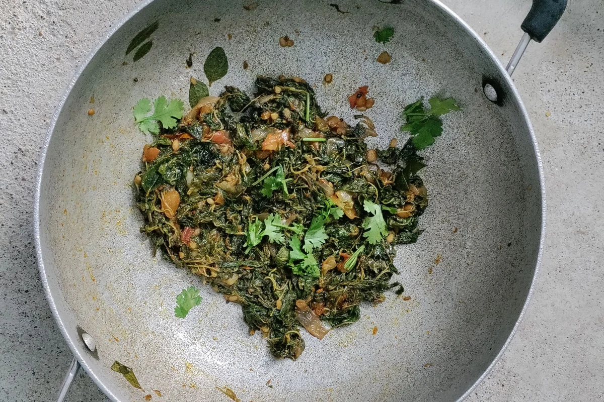 A deep kadai filled with cooked greens