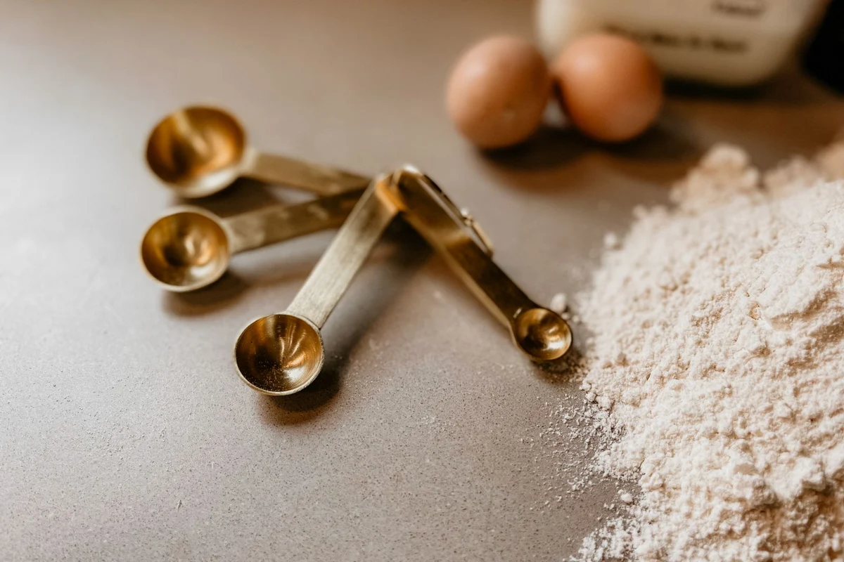 Measuring spoons beside flour and eggs