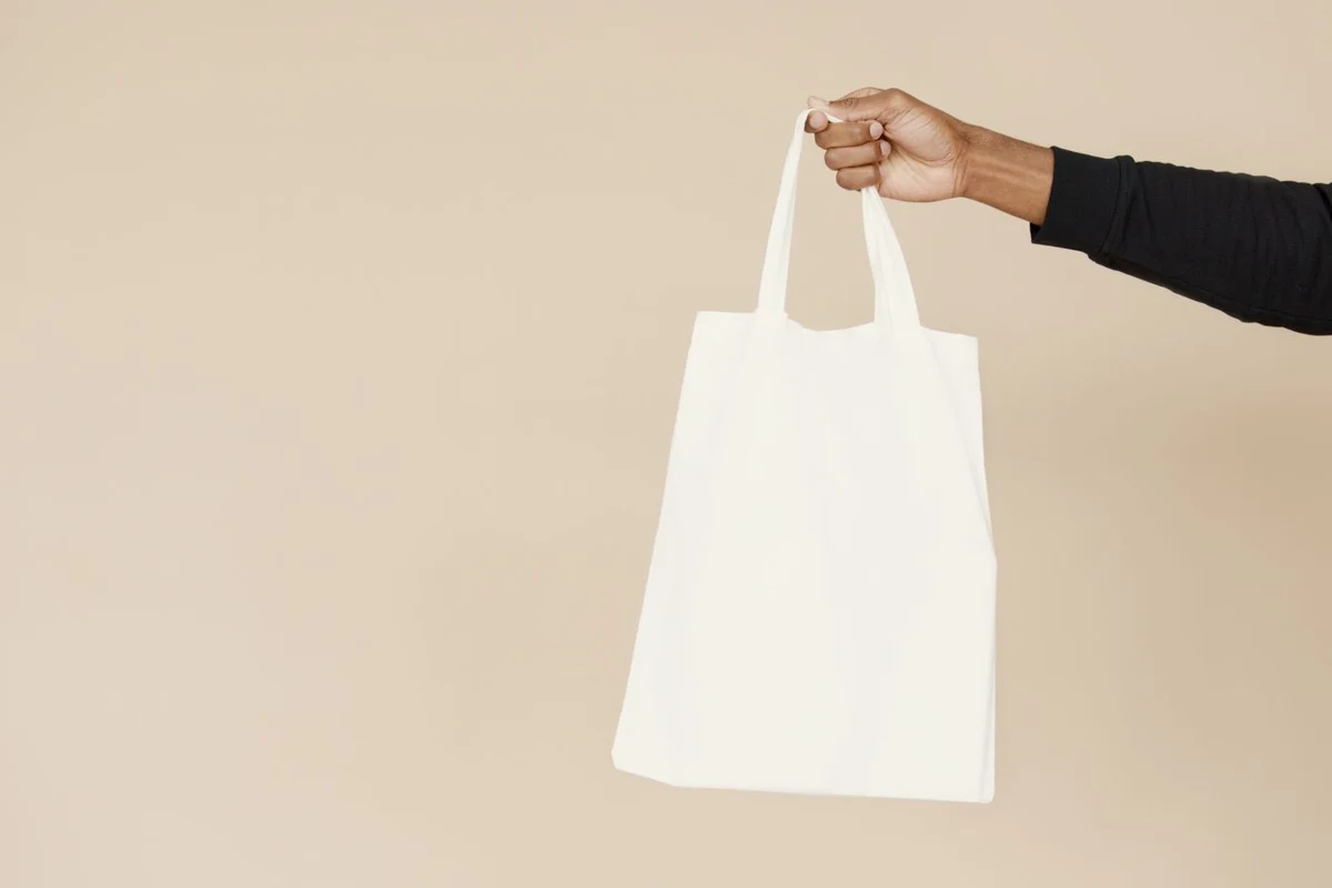 A reusable fabric shopping bag held by its handles