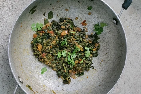 A deep kadai filled with cooked greens